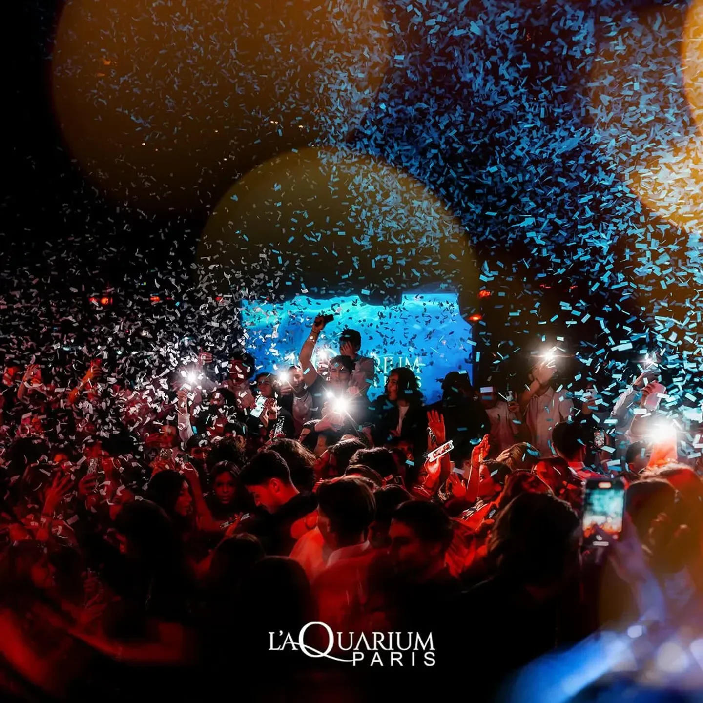 Energetic crowd celebrating at L'Aquarium Club in Paris with confetti and flashing lights.