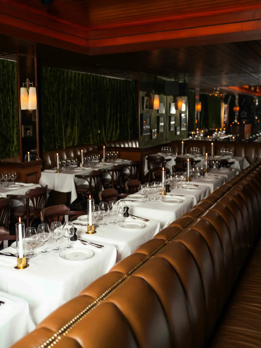 Elegant dimly lit dining room interior at Le Pompon restaurant with candlelit tables and leather banquettes.